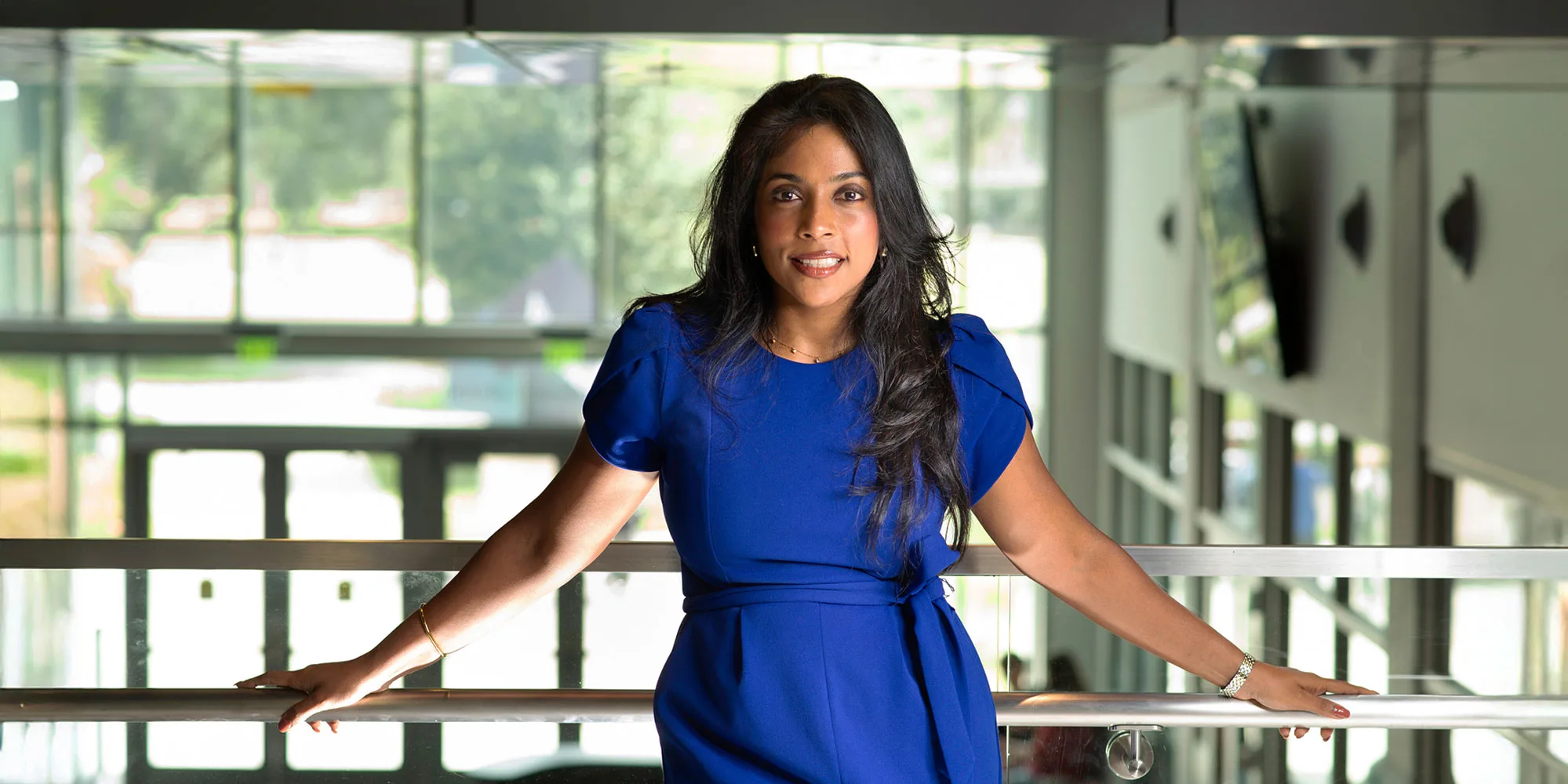 Sarah Jayasekaran standing at a railing inside a university building.