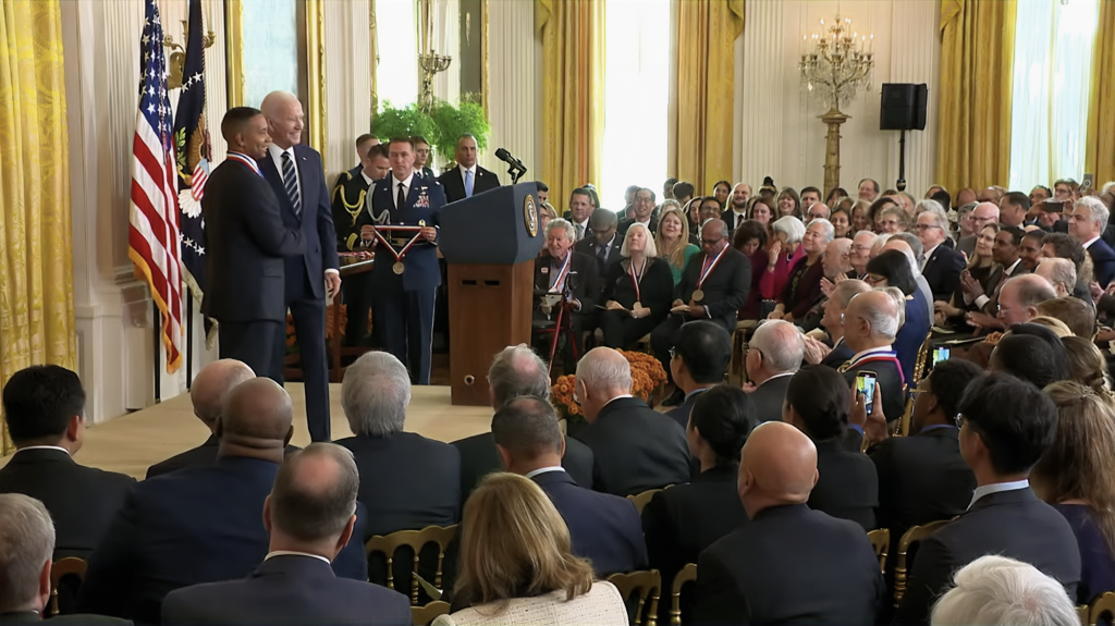 Image of National Medal of Technology and Innovation Laureate Juan E. Gilbert, PH.D., chair of the University of Florida Department of Computer & Information Science & Engineering, shaking hands with U.S. President Joe Biden in a room full of people attending a medal ceremony.