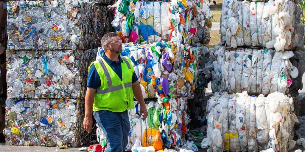 A worker walks past bales of recycled plastic bottles, aluminum and paper at the Leveda Brown Environmental Park and Transfer Station in Gainesville. [Doug Engle/Ocala Star-Banner]