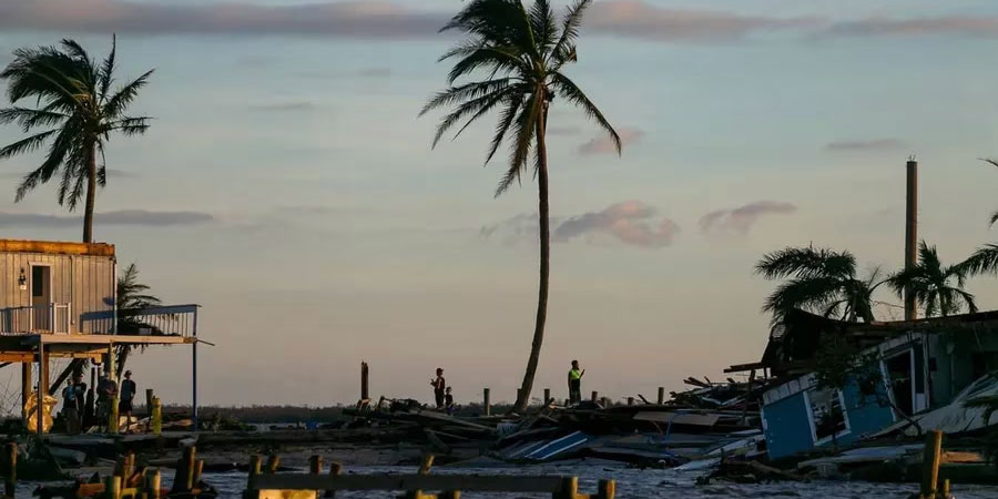 People are seen near damaged properties on a broken section of Pine Island Road on Thursday, Sept. 29, 2022, in Matlacha, Fla. Hurricane Ian made landfall on the coast of South West Florida as a category 4 storm Tuesday afternoon leaving areas affected with flooded streets, downed trees and scattered debris. [ MATIAS J. OCNER | Miami Herald ]