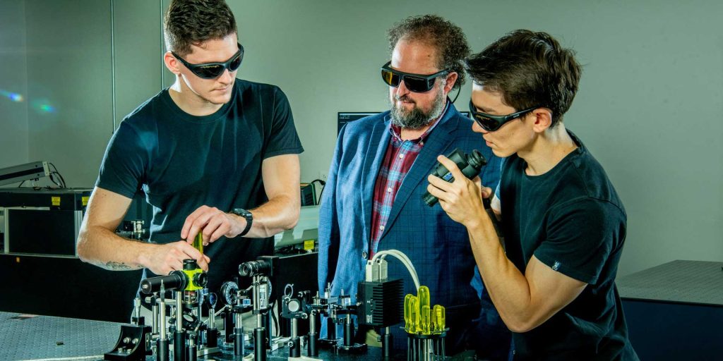 Kyle Hartig works with two grad assistants on machinery in his research lab.