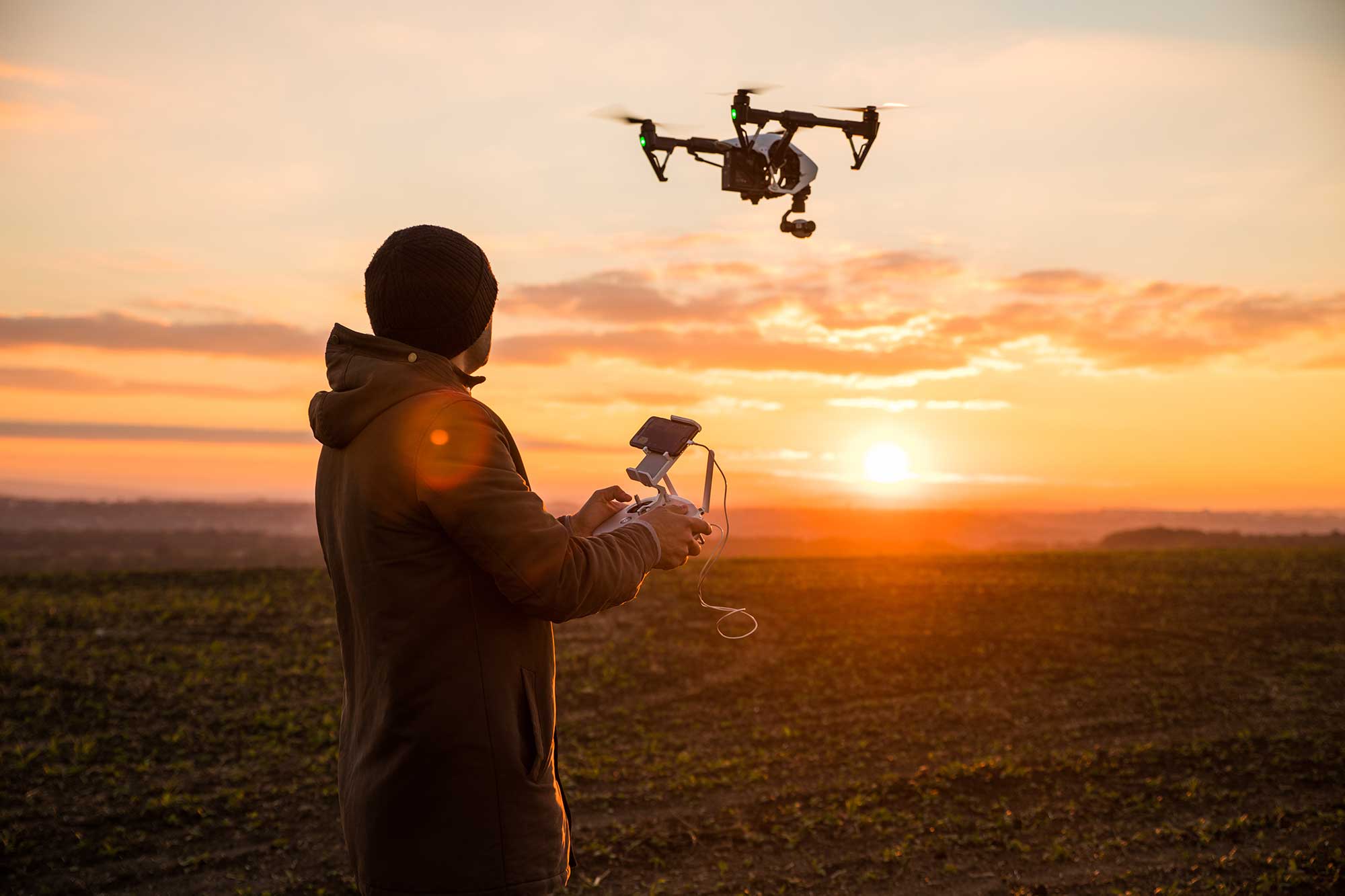Man operating a drone with remote control. Dark silhouette against colorful sunset. Soft focus.