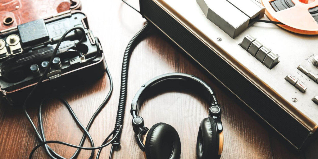Headphones and a twentieth century tape recorder sit on a desk.