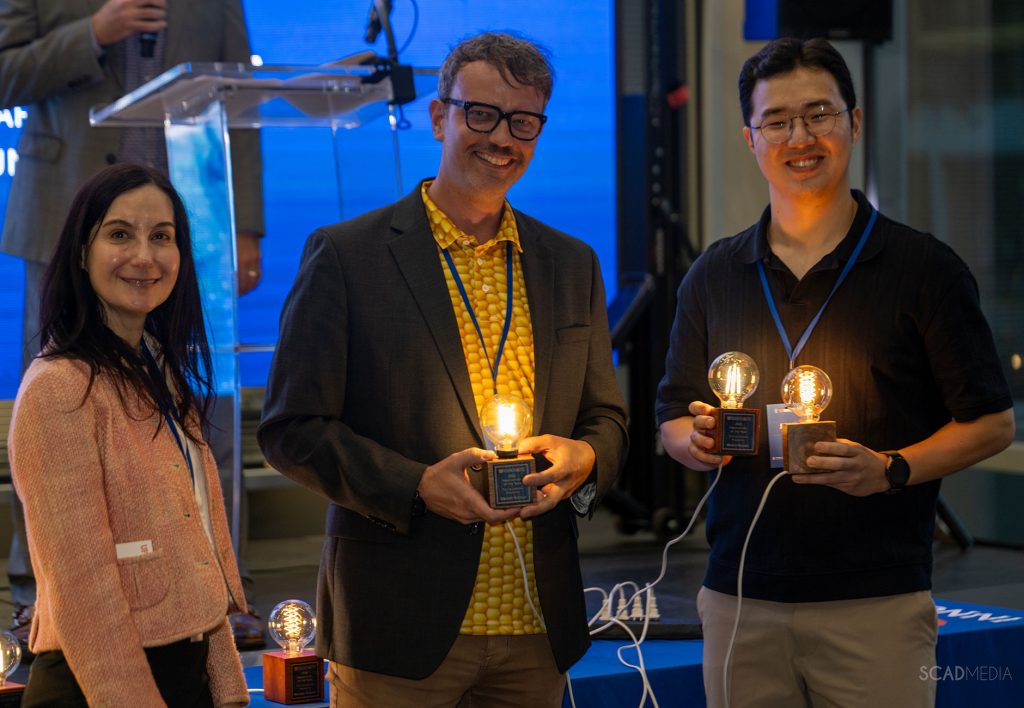 Gregory Hudalla, Ph.D., from the J. Crayton Pruitt Family Department of Biomedical Engineering and Junha Park receive their award for their ELISA test speeds project from Melissa Kuchma from UF Innovate.