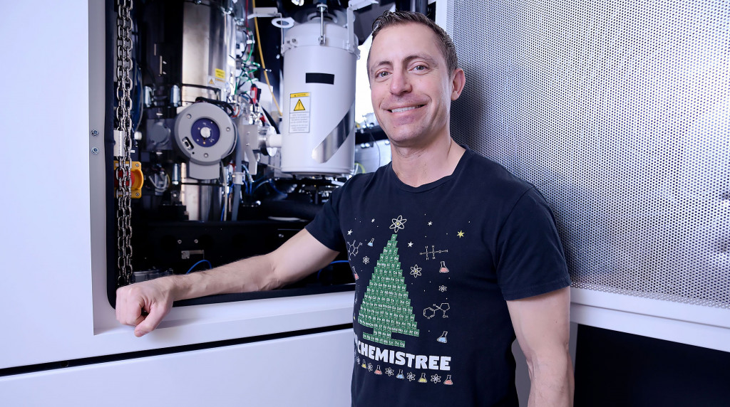 Portrait of Nicholas Rudawski, standing in front of an equipment in a lab.