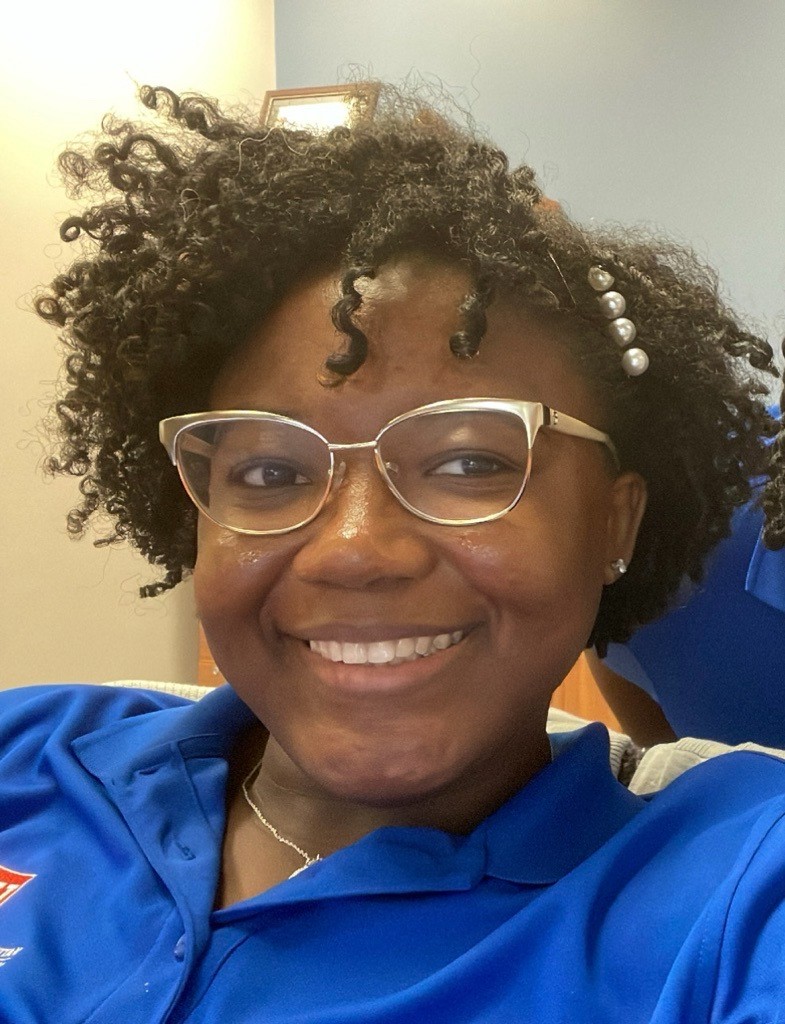 A woman with black, curly hair smiling for a headshot photo. 