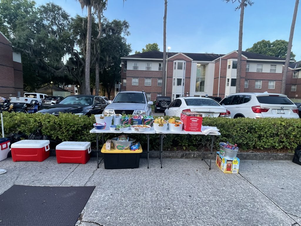 A picture of folding tables with snacks on them and coolers on he ground. 