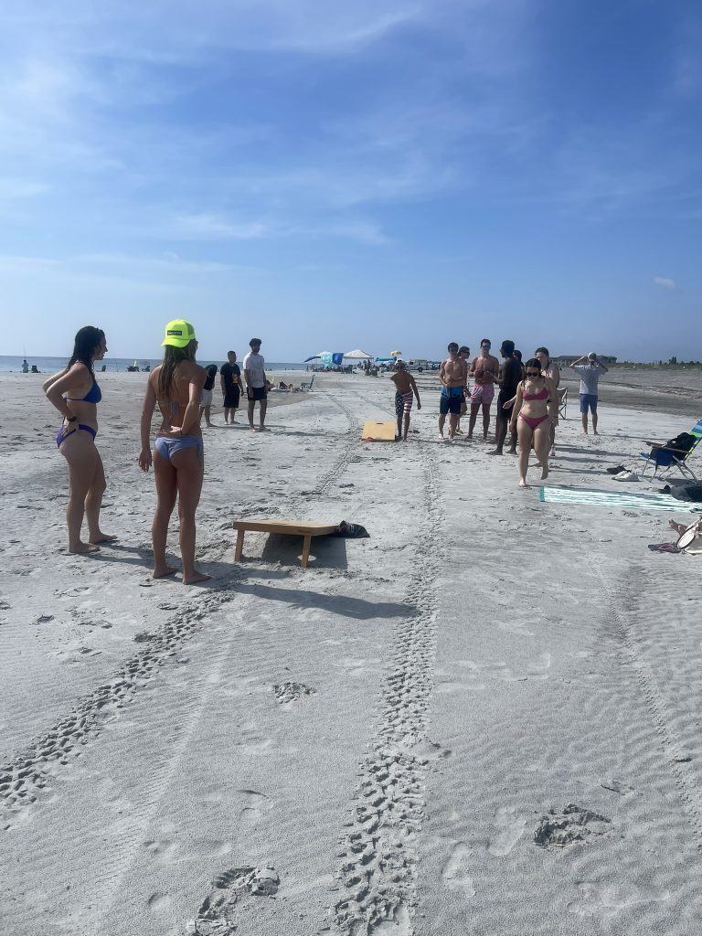 A group of students standing around and waiting their turn during corn hole. 