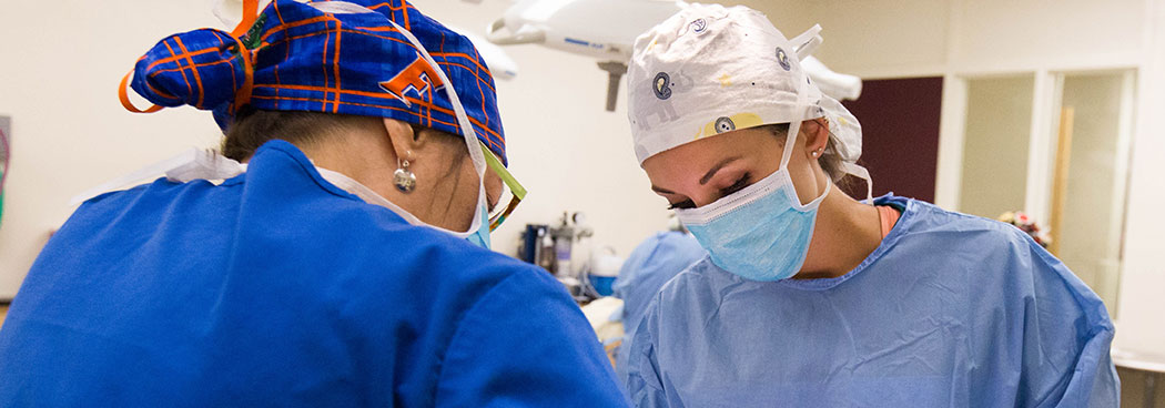 Photo of 2 female health care providers wearing PPE and performing a procedure on an unseen patient