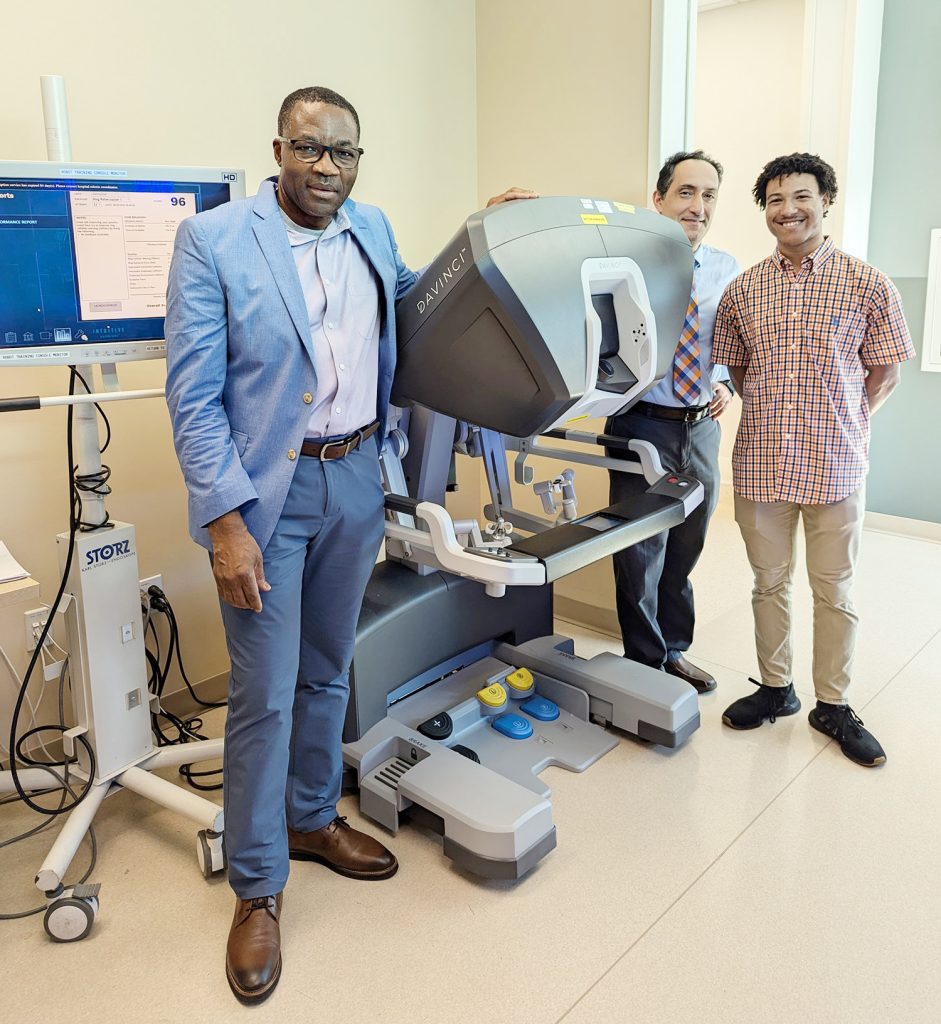 Christophe Bobda, Ph.D., left, UF professor and surgeon Ali Zarrinpar, and Ph.D. student Antonio Hendricks pose next to a Da Vinci SimNow robotic-surgery simulator.